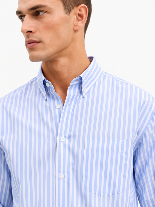 A close-up of a man wearing a light blue and white vertically striped button-down shirt against a plain white background.