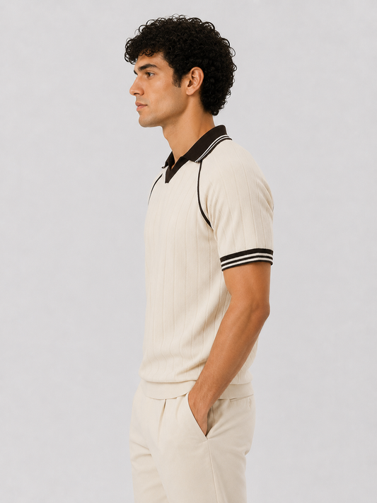 A man in side profile wearing a cream-colored ribbed short-sleeve polo shirt with black trim on the collar and sleeve cuffs, paired with matching cream trousers, against a light gray studio background.